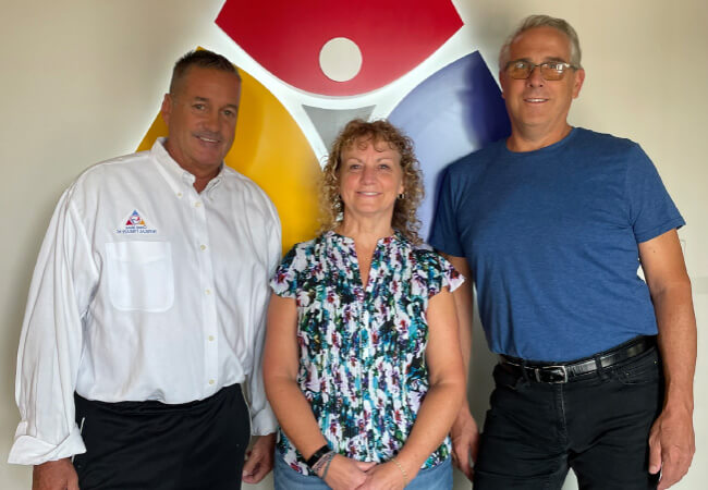 3 individuals standing side-by-side in front of the Trilogy PT logo.