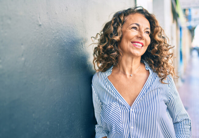 A woman standing against a blue wall, smiling, after having a total shoulder replacement.